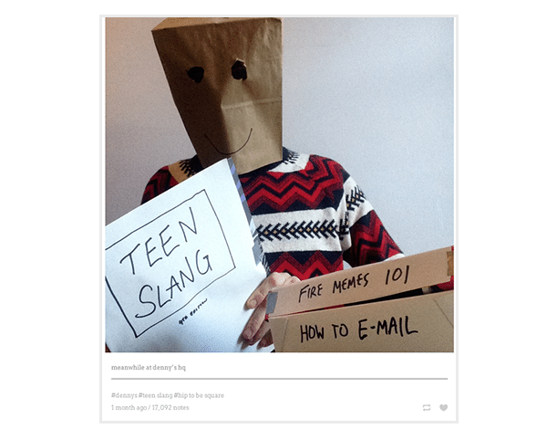 An image of a male Denny's employee with a smiling paper bag over his head holds signs saying "teen slang", "fire memes 101" and "how to e-mail"